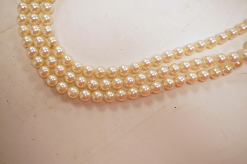 A cultured pearl, ruby and diamond clasp, composed of three rows of cultured pearls measuring approximately 6.9mm diameter, to a white precious metal (tests as 14k) disc-shaped clasp pavé-set with brilliant-cut diamonds